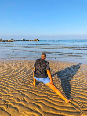 Bir adam spor yapmaya gider, deniz kıyısında egzersiz yapar.