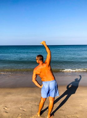 Bir adam spor yapmaya gider, deniz kıyısında egzersiz yapar.