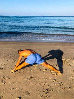 Bir adam spor yapmaya gider, deniz kıyısında egzersiz yapar.