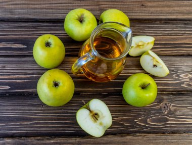 Ahşap zemin üzerinde elma suyu olan yeşil elma ve sürahi.