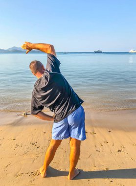 Bir adam spor yapmaya gider, deniz kıyısında egzersiz yapar.