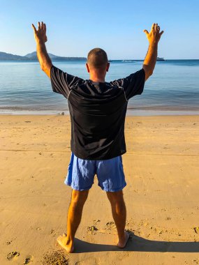 Bir adam spor yapmaya gider, deniz kıyısında egzersiz yapar.