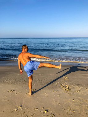 Bir adam spor yapmaya gider, deniz kıyısında egzersiz yapar.