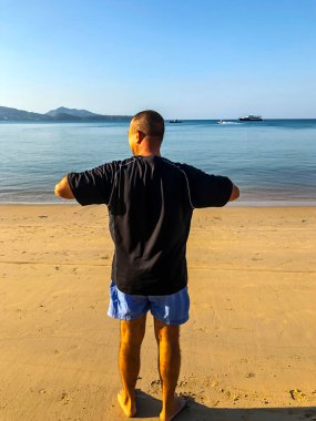 Bir adam spor yapmaya gider, deniz kıyısında egzersiz yapar.