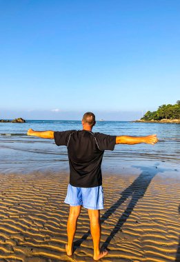 Bir adam spor yapmaya gider, deniz kıyısında egzersiz yapar.