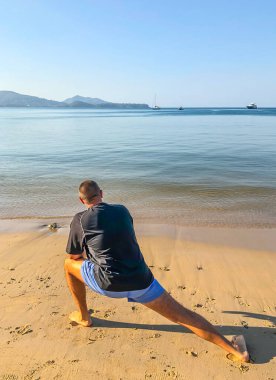 Bir adam spor yapmaya gider, deniz kıyısında egzersiz yapar.