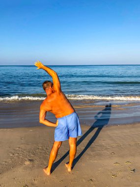 Bir adam spor yapmaya gider, deniz kıyısında egzersiz yapar.