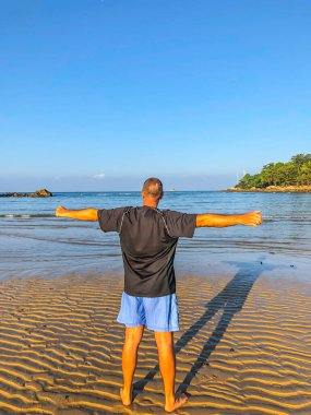 Bir adam spor yapmaya gider, deniz kıyısında egzersiz yapar.