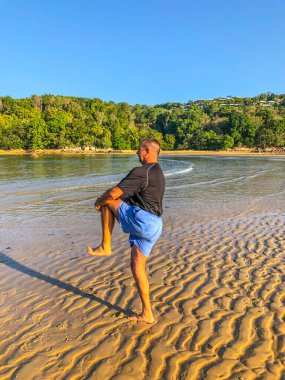 Bir adam spor yapmaya gider, deniz kıyısında egzersiz yapar.