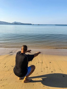 Bir adam spor yapmaya gider, deniz kıyısında egzersiz yapar.