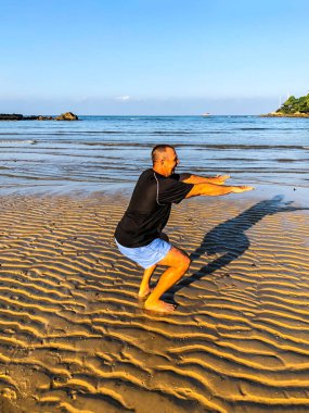 Bir adam spor yapmaya gider, deniz kıyısında egzersiz yapar.