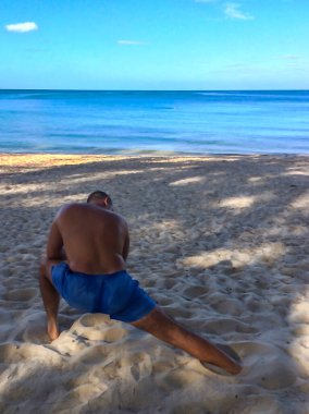 Bir adam spor yapmaya gider, deniz kıyısında egzersiz yapar.