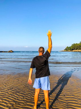 Bir adam spor yapmaya gider, deniz kıyısında egzersiz yapar.