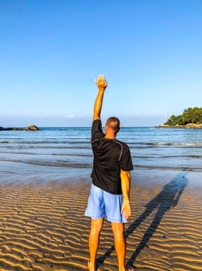 Bir adam spor yapmaya gider, deniz kıyısında egzersiz yapar.