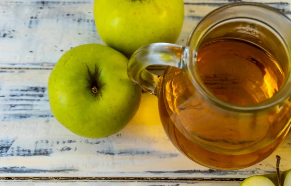 Ahşap zemin üzerinde elma suyu olan yeşil elma ve sürahi.