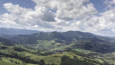 Dağ manzarasının zamanlaması beyaz, hızlı hareket eden bulutlar, yeşil alanlar ve mavi dağlarla