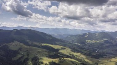Dağ manzarasının zamanlaması beyaz, hızlı hareket eden bulutlar, yeşil alanlar ve mavi dağlarla