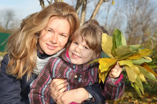Sarı saçlı kadın, anne ve kız sarı ve yeşil sonbahar yapraklı.