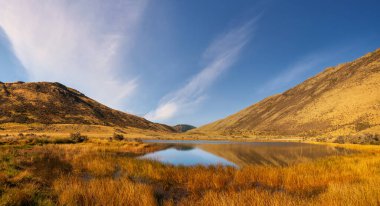 Grassy autumn colours and dry barren hills surrounding a remote little lake in the Canterbury high country