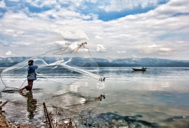 SUMATERA - FEBRUARY 10: A fisherman casts his net into Lake Singkarak, a tectonic lake in Sumatera, Indonesia on Feb 10, 2012. It is the biggest lake in Sumatera measuring 20km long and 8km wide. clipart