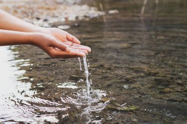 Doğanın ortasında bir kadının eli suya dokunuyor.