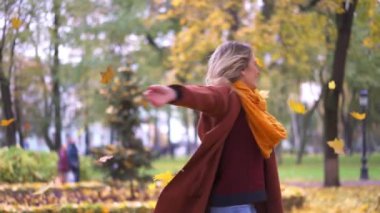 Güzel genç bir kadın sonbaharda bahçede ya da parkta düşen sarı yaprakların altında kamera için kıvrılır. Güz yapraklarındaki güzel, gülümseyen genç kadın..