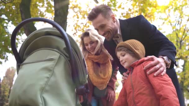Caminando en un parque de otoño familia joven con un bebé recién nacido en un cochecito. Familia al aire libre en un parque de otoño dorado. Imagen teñida — Vídeos de Stock
