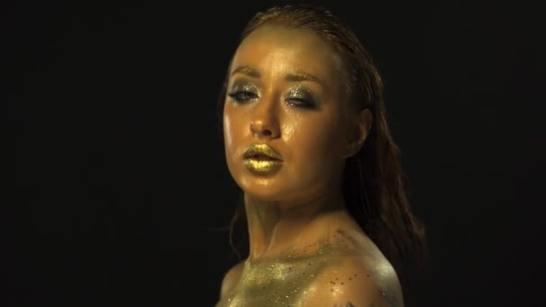 Golden Girl Turning to Camera, Blowing Gold Glitter Confetti and Winking an Eye , Golden Skin, Golden Make-up, Golden Lipstick, Slow Motion, Close-up, Black Background — Wideo stockowe