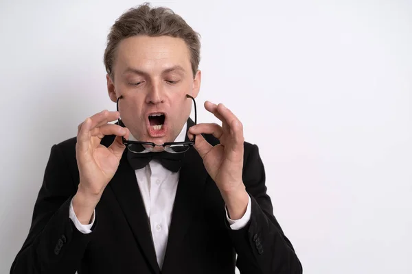 Cleaning glasses. Successful young businessman in tuxedo proud of himself, fixing his eye glasses. Half-length portrait of a handsome man in standing against the white background — Stock Photo, Image