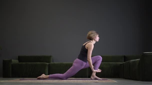 Samotna kobieta w odzieży sportowej robiąca boczne deski w przestronnym studiu jogi. Sportowa kobieta ćwiczy Hatha Jogę. Pełna długość. Szare tło — Wideo stockowe