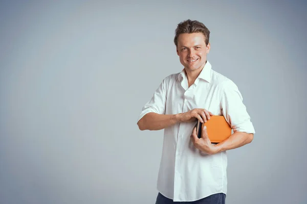 Mosolygó szabadúszó férfi fehér ingben, narancssárga füzetet vagy naplót tartva elszigetelve fehér háttérrel vagy az irodában. Egy pozitív fiatal üzletember portréja, aki a naplóját tartja. — Stock Fotó