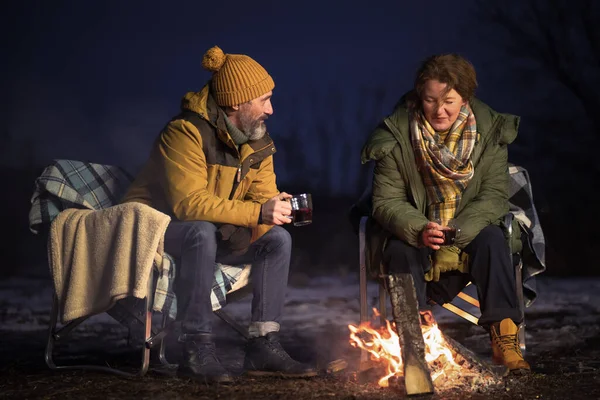在爱情成熟的夫妻浪漫的晚餐在篝火边喝着热的天然茶 坐在毛毯上过冬 夫妇俩坐在雪中篝火边 家庭假期和旅行概念 — 图库照片