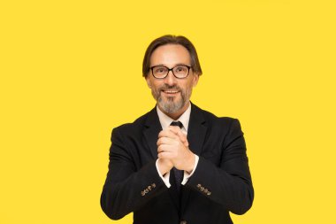 Gesturing All The Best with hands handsome middle aged businessman looking at camera isolated on yellow background. Handsome mature businessman in black suit and eye glasses. Business concept.
