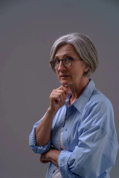 Dramatic portrait of an mature grey haired woman. Grey haired mature woman studio shot in low light. Sad lonely mature woman. Senior woman thinking in low light.