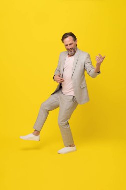 Orta yaşlı iş adamı müzisyen sarı arka planda mutlu bir şekilde gitar çalıyormuş gibi yapıyor. Beyaz takım elbiseli yakışıklı bir iş adamı. İş konsepti. Müzik konsepti. 