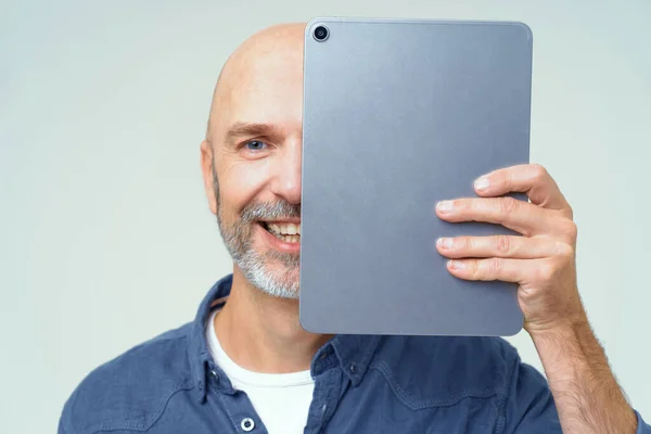 Przystojny Śmiały Mężczyzna Zakrywa Połowę Twarzy Cyfrowym Tabletem Ręku Uśmiechając — Zdjęcie stockowe