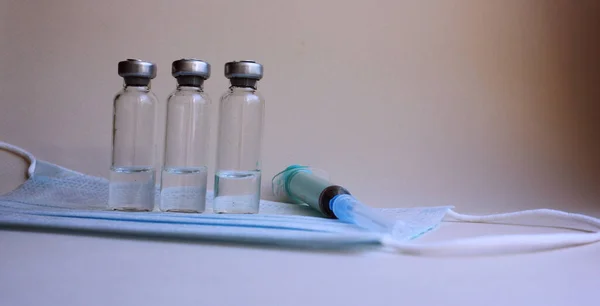 Eine Spritze mit Nadel, Medikamentenflaschen liegen auf einer medizinischen Maske auf hellem Hintergrund. Diktate und Immunität. Impfungen gegen Virusinfektionen. Medikament und Injektion. Injektion, Medikament. Kopierraum. — Stockfoto