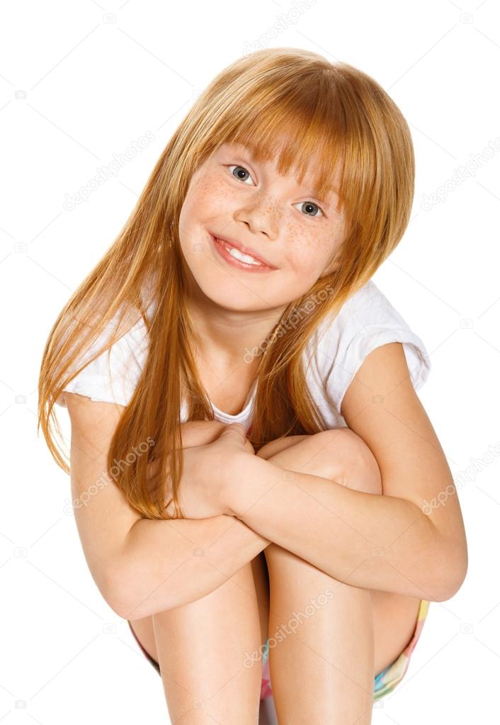 A cheerful little girl with red hair is sitting. isolated on the white background