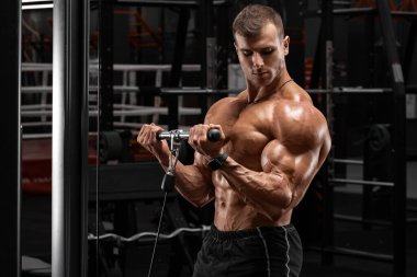 Spor salonundaki kaslı adam pazılar için egzersiz yapıyor, spor yapıyor. Güçlü erkek çıplak gövde kasları