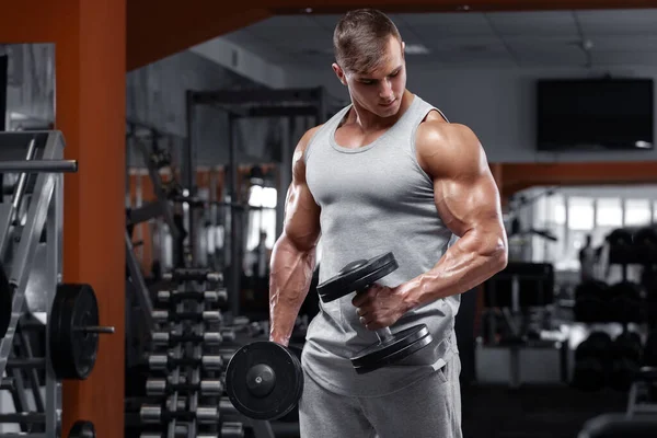 Spor salonunda egzersiz yapan kaslı bir adam. Halterlerle egzersiz yapıyor. Güçlü bir erkek.