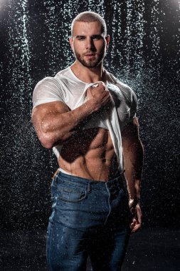 Muscular man under the rain in studio. Sexy male in water drops, abs
