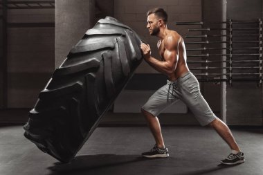 Kaslı adam lastik, güçlü erkek çıplak gövde saygısız spor salonunda egzersiz