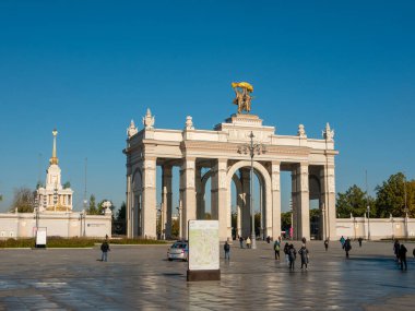 Moskova, Rusya - 5 Ekim 2021: VDNKh 'nin ana girişinin kemeri mavi gökyüzünün arka planına karşı. İnsanlar bir sonbahar günü parkın girişindeki meydanda yürürler..