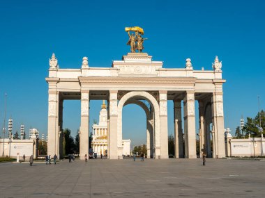 Moskova, Rusya - 5 Ekim 2021: VDNKh 'nin ana girişinin kemeri mavi gökyüzünün arka planına karşı. İnsanlar güneşli bir sonbahar gününde parkın girişindeki meydanda yürürler..