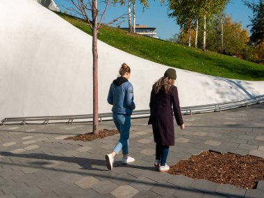 Moskova, Rusya - 5 Ekim 2021 Zaryadye Parkı. Aydınlık ve güneşli bir sonbahar gününde kızlar yaya yolunda yürürler..