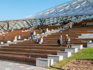 Moskova, Rusya - 5 Ekim 2021 Zaryadye Parkı. İnsanlar güneşli bir sonbahar gününde Zaryadye konser salonunun amfi tiyatrosunun sıralarında otururlar..