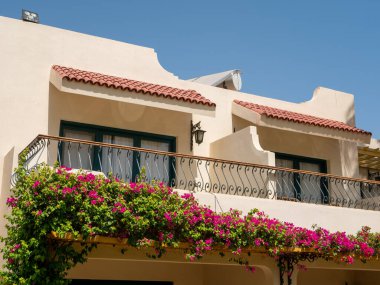 Hurghada, Mısır- 22 Eylül 2021: otelin iki katlı evleri. Balkon mavi gökyüzüne karşı parlak pembe çiçeklerle süslenmiş. Yakın plan..