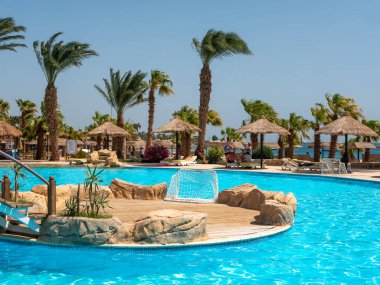 Hurghada, Mısır- 22 Eylül 2021: temiz mavi suyla otel havuzu manzarası. İnsanlar rahatlar ve havuzun etrafında güneşlenirler..