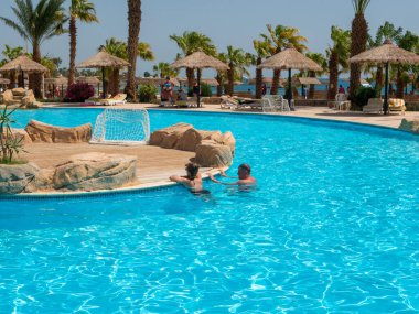 Hurghada, Mısır- 22 Eylül 2021: temiz mavi suyla otelin havuzunun manzarası. İnsanlar güneşlenirler, dinlenirler ve mavi gökyüzünün arka planına karşı havuzda yüzerler..
