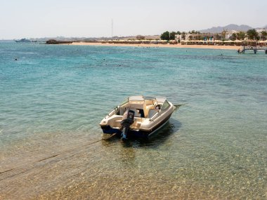 Hurghada, Mısır - 22 Eylül 2021: Palmiye ağaçlı bir Mısır kumlu plajının zeminine demirlemiş bir motorlu tekne görüntüsü.